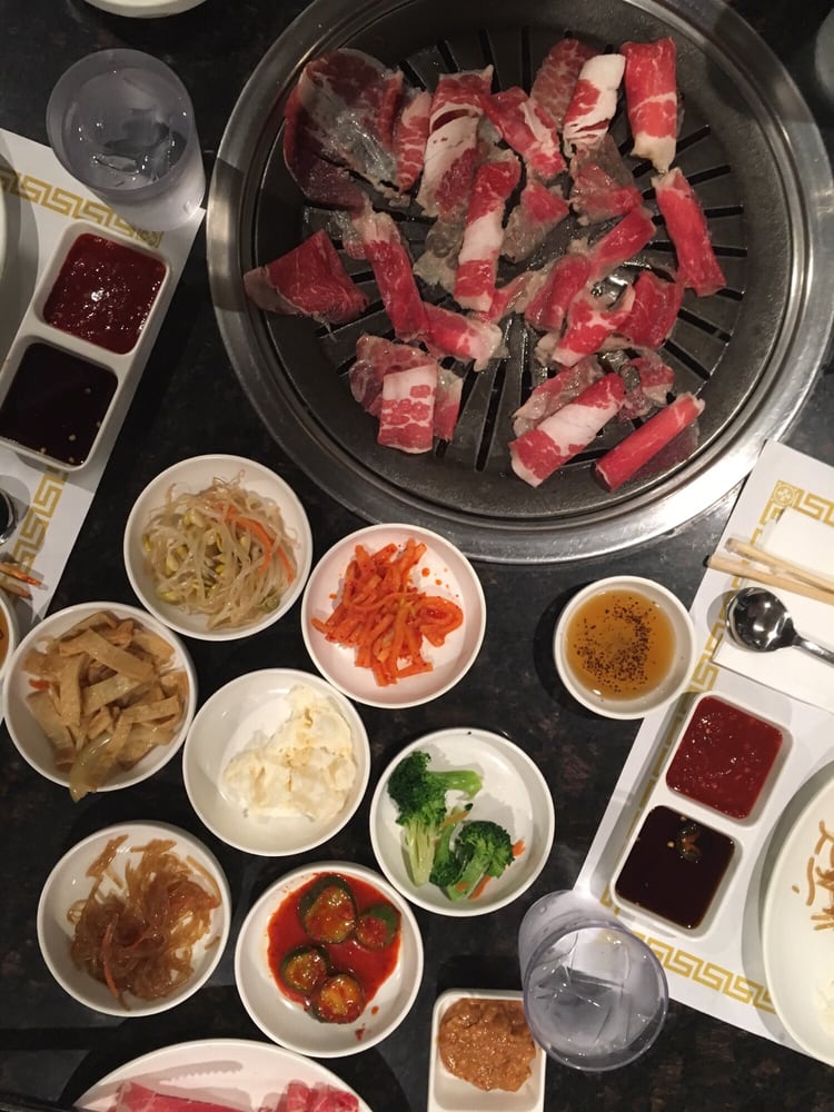 Raw beef on the grill surrounded by banchan and dipping sauces